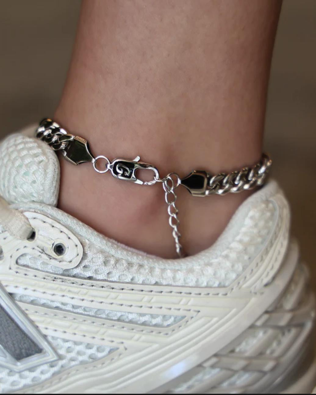 Close-up of a person wearing a silver Cuban Link Anklet with a blurred background