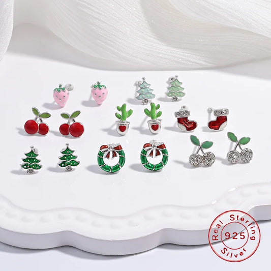 A collection of children's jewelry featuring studs in the shapes of cherries, strawberries, and festive trees, with a white and green color scheme.
