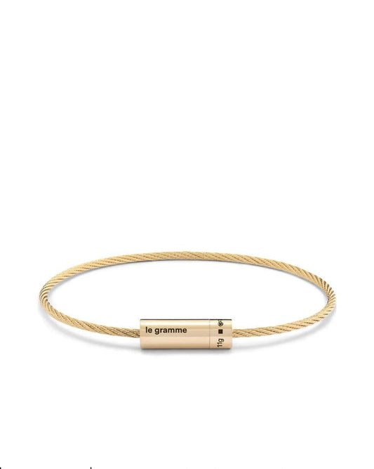 Gold bracelet with cylindrical gold tag on a white background