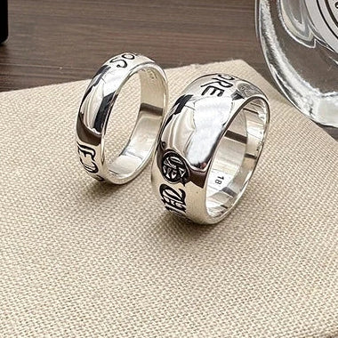 Two silver rings with engraved designs on a textured surface