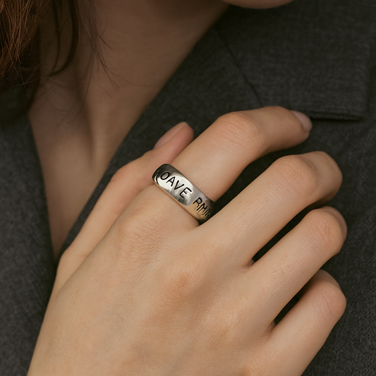 Silver ring with engraved text on a person's finger against a dark background