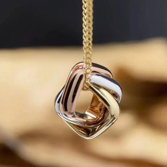 Gold and rose gold knot-shaped pendant on a chain against a blurred background