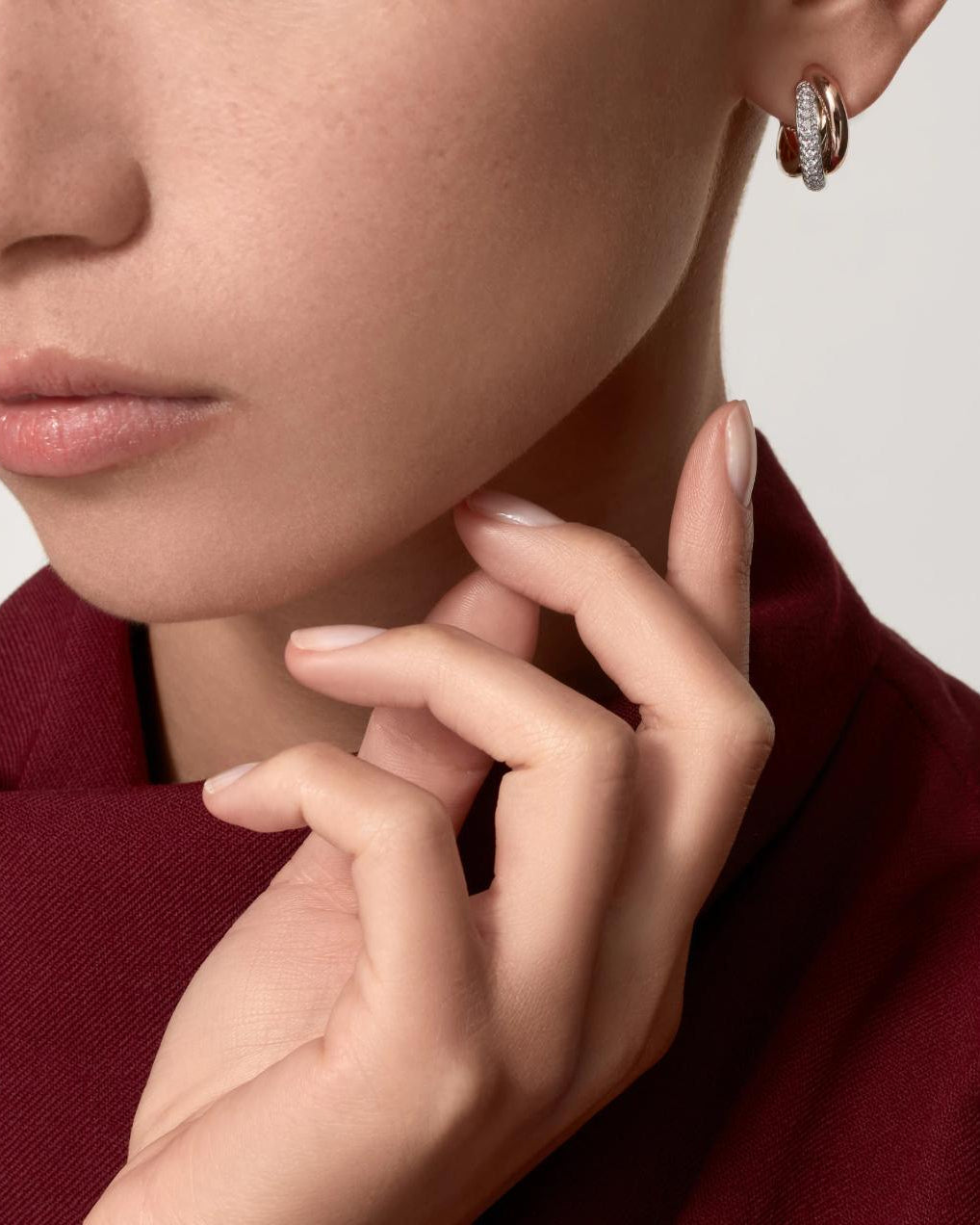 A sophisticated woman in a brown leather shirt gracefully adjusting her collar, wearing the classic Harmonie Trio 18K tri-color gold-plated silver earrings.