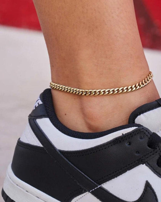 Close-up of a person wearing a gold Cuban Link Anklet with a blurred background