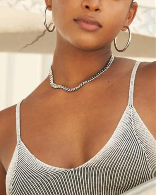 Woman wearing a cuban link necklace with thin straps, standing by a railing.
