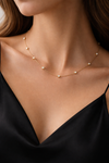 An elegant woman in a black silk dress wearing the Auréclaire 18K gold-plated 925 silver station necklace, featuring brilliant bezel-set moissanite stones draped delicately across her collarbone.