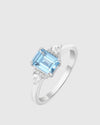 Angled studio shot of the Aerion Celestia ring showcasing the 5.44-carat natural sky blue topaz flanked by pear and round-cut lab-grown diamonds on a rhodium-plated 925 silver band.