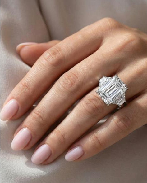 A close-up of an elegant woman's hand resting on her shoulder, modeling the breathtaking 6-carat total weight emerald-cut moissanite engagement ring in solid 925 silver.
