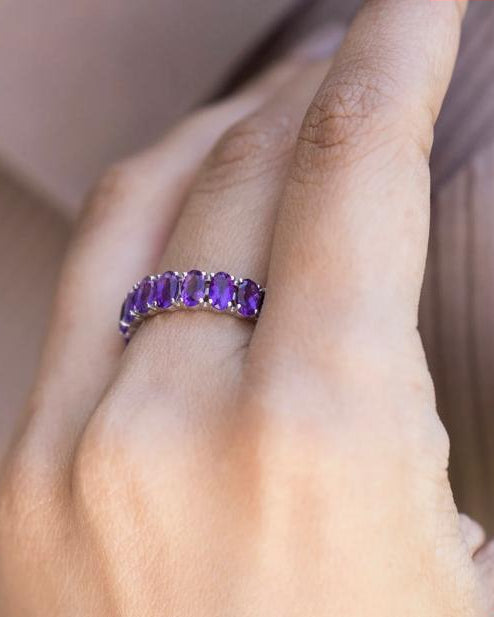 A woman's hand elegantly wearing the Améthra 925 silver eternity ring, showcasing a continuous row of deep violet natural African amethysts.