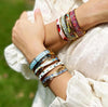 Close-up of a person's arm wearing multiple colorful bracelets with a blurred green background.