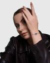 A sophisticated woman in a dark leather jacket elegantly posing with her hand near her face, wearing the Aerion Oculus solid 925 silver protective talisman bracelet featuring a 1-carat black moissanite center stone.