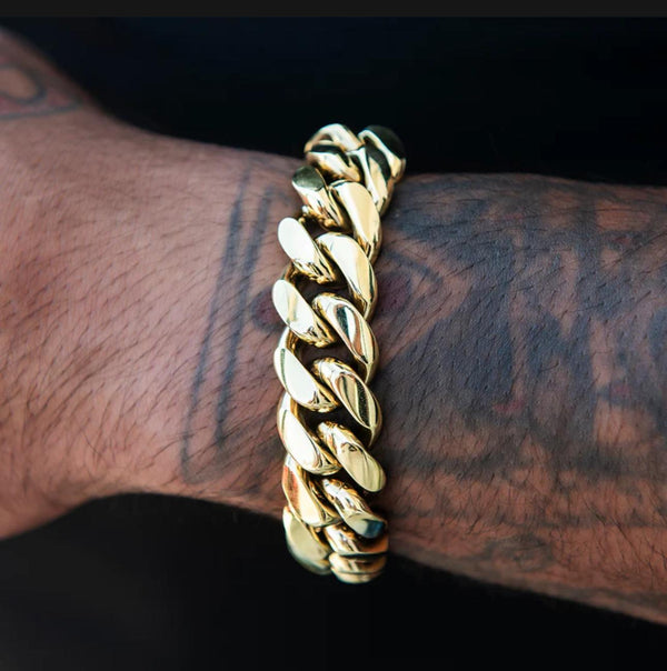 Gold chain bracelet on a wrist with tattoos against a dark background