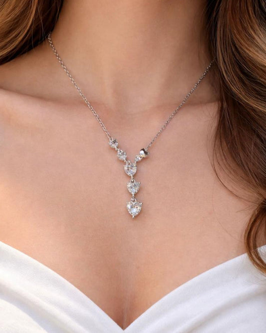 A close-up of a woman in a white plunging neckline dress wearing the ultra-lightweight Cœur Cascade Y-pendant necklace, showcasing its flawless diamond-like sparkle and romantic drape.