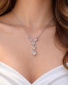 A close-up of a woman in a white plunging neckline dress wearing the ultra-lightweight Cœur Cascade Y-pendant necklace, showcasing its flawless diamond-like sparkle and romantic drape.