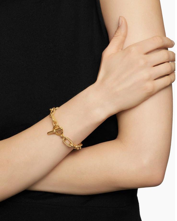 A sophisticated female model wearing a black off-shoulder top, styling the Claspéra Madison 11mm chunky gold chain bracelet with the toggle clasp.