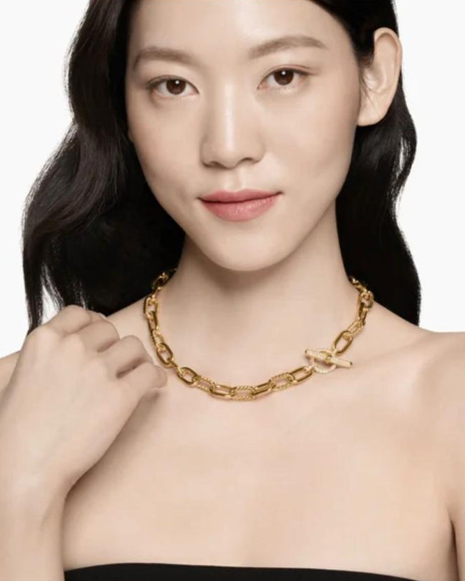 A sophisticated female model wearing a black off-shoulder top, styling the Claspéra Madison 11mm chunky gold chain necklace with the diamond-paved toggle clasp resting elegantly on her collarbone.
