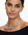 A sophisticated female model wearing a black off-shoulder top, styling the Claspéra Madison 11mm chunky 925 silver chain necklace with the diamond-paved toggle clasp resting elegantly on her collarbone.