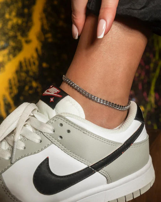 Close-up of a person wearing a silver Cuban Link Anklet with a blurred background