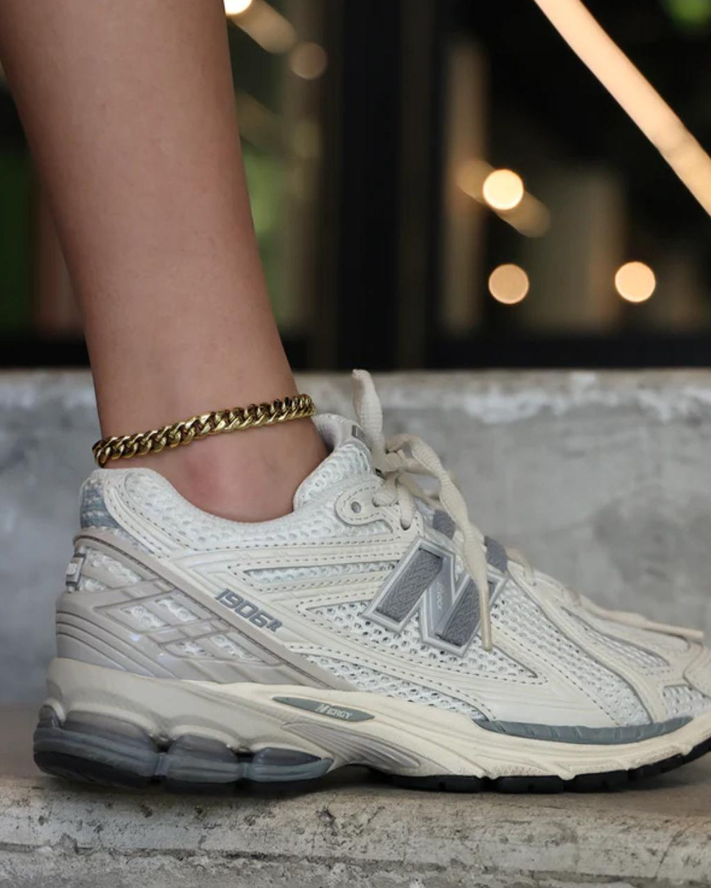 Close-up of a person wearing a gold Cuban Link Anklet with a blurred background