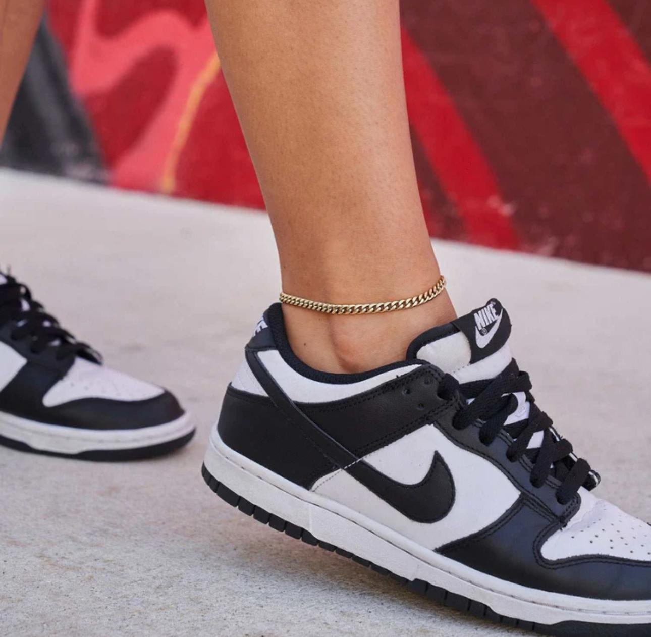 Close-up of a person wearing a gold Cuban Link Anklet with a blurred background