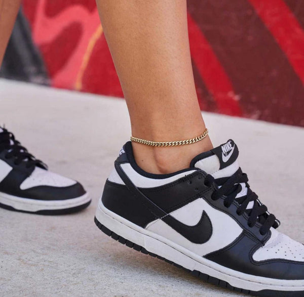 Close-up of a person wearing a gold Cuban Link Anklet with a blurred background