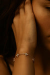 A close-up of a sophisticated female model with her hand resting near her face, wearing the delicate Fiorella 1.8g solid 925 silver station bracelet featuring brilliant four-petal moissanite flower motifs.