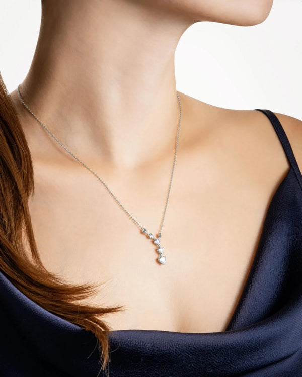 A sophisticated woman in a dark navy silk dress modeling the Cœur Cascade 925 silver Y-pendant necklace, elegantly elongating her neckline with brilliant heart-cut stones.