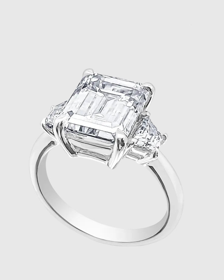 Angled studio shot of the 18K white gold-plated 925 silver ring, highlighting the massive 5-carat emerald-cut moissanite and the flawless tapered baguette side stones.