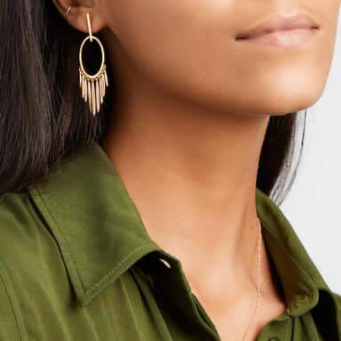 Close-up of a person wearing gold fringe earrings with a green shirt.
