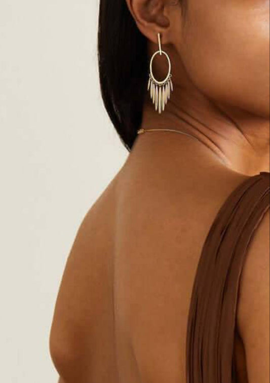 Close-up of a person wearing a hoop earring with fringe details on a neutral background
