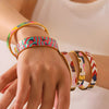 Hand wearing multiple colorful bracelets on a light background