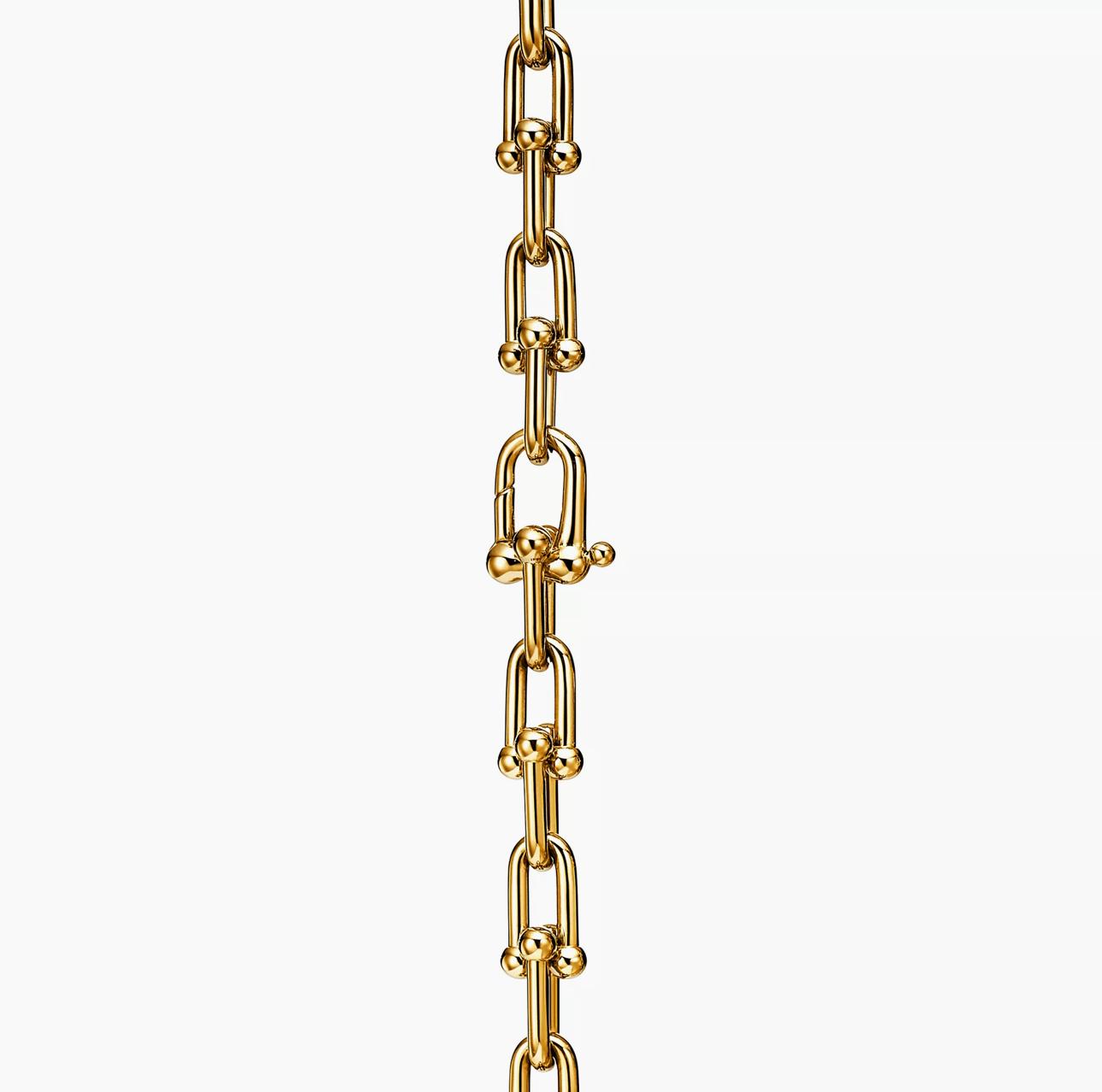 Close-up of a gold horseshoe-link chain showing the hidden push-lock clasp integrated within the rounded links.