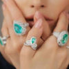 Close-up of a hand wearing multiple rings with green gemstones and silver bands.