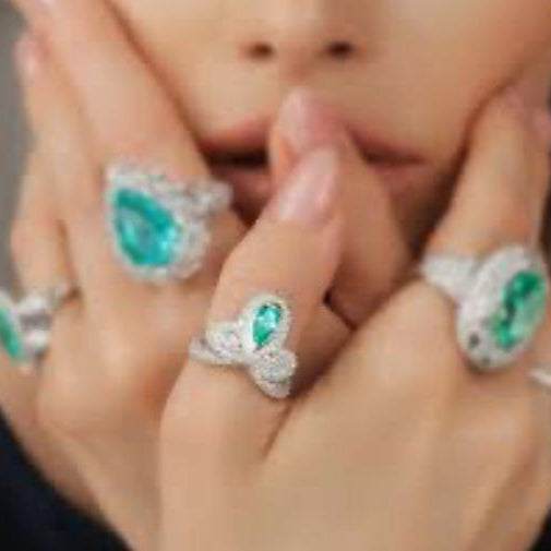 Close-up of a hand wearing multiple rings with green gemstones and silver bands.