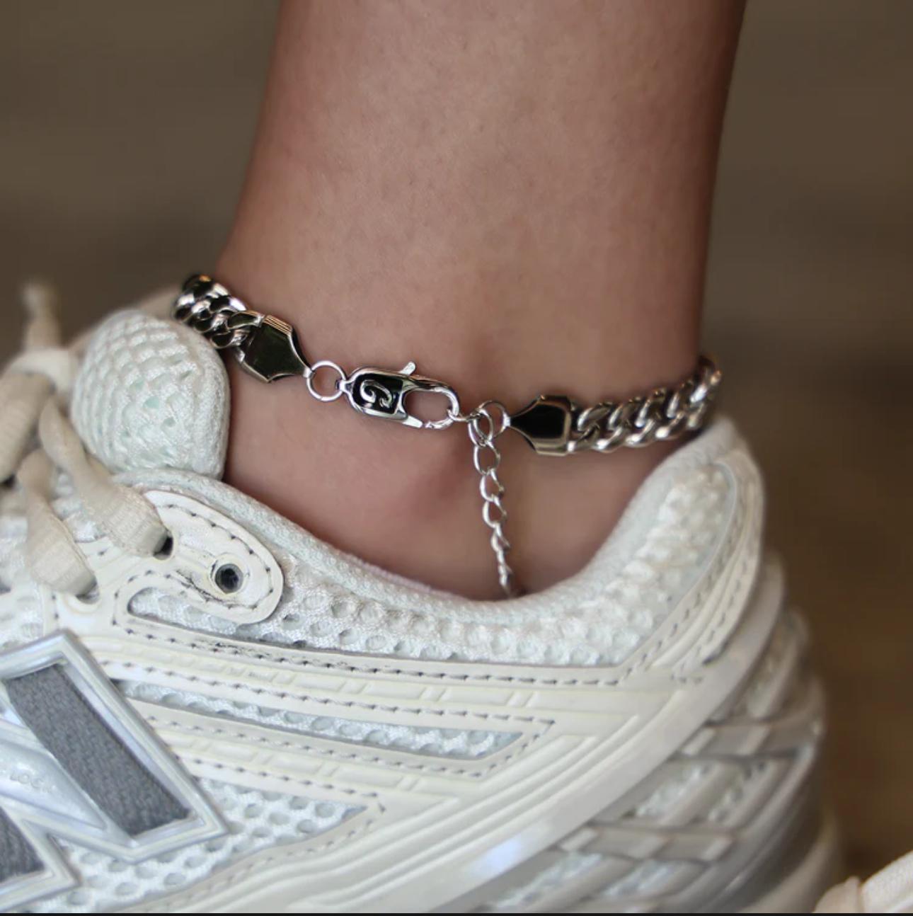 Close-up of a person wearing a silver Cuban Link Anklet with a blurred background