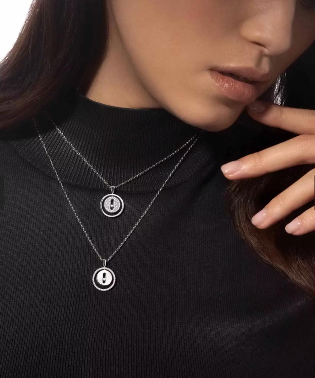 Woman wearing a black turtleneck with two silver necklaces featuring circular pendants.