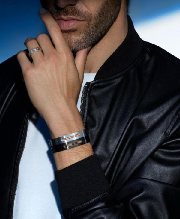 Person wearing a silver bracelet and ring, with a black jacket against a blue background