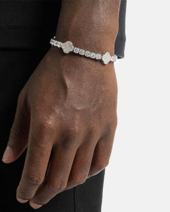 A man wearing a black outfit modeling the Aerion Trèfle massive 20g solid 925 silver tennis bracelet, featuring brilliant 4mm moissanite stones and pavé clover motifs on his wrist.