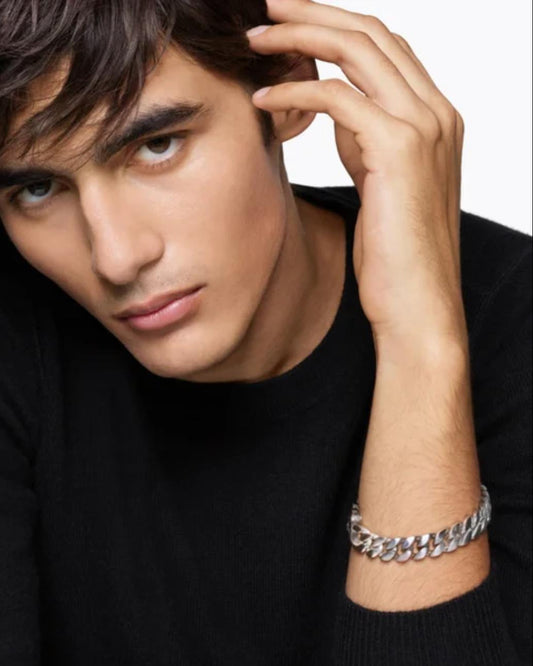 A handsome male model in a black cashmere sweater wearing the bold 11.5mm Aventino solid 925 silver Cuban curb link bracelet on his wrist, exuding quiet masculine luxury.