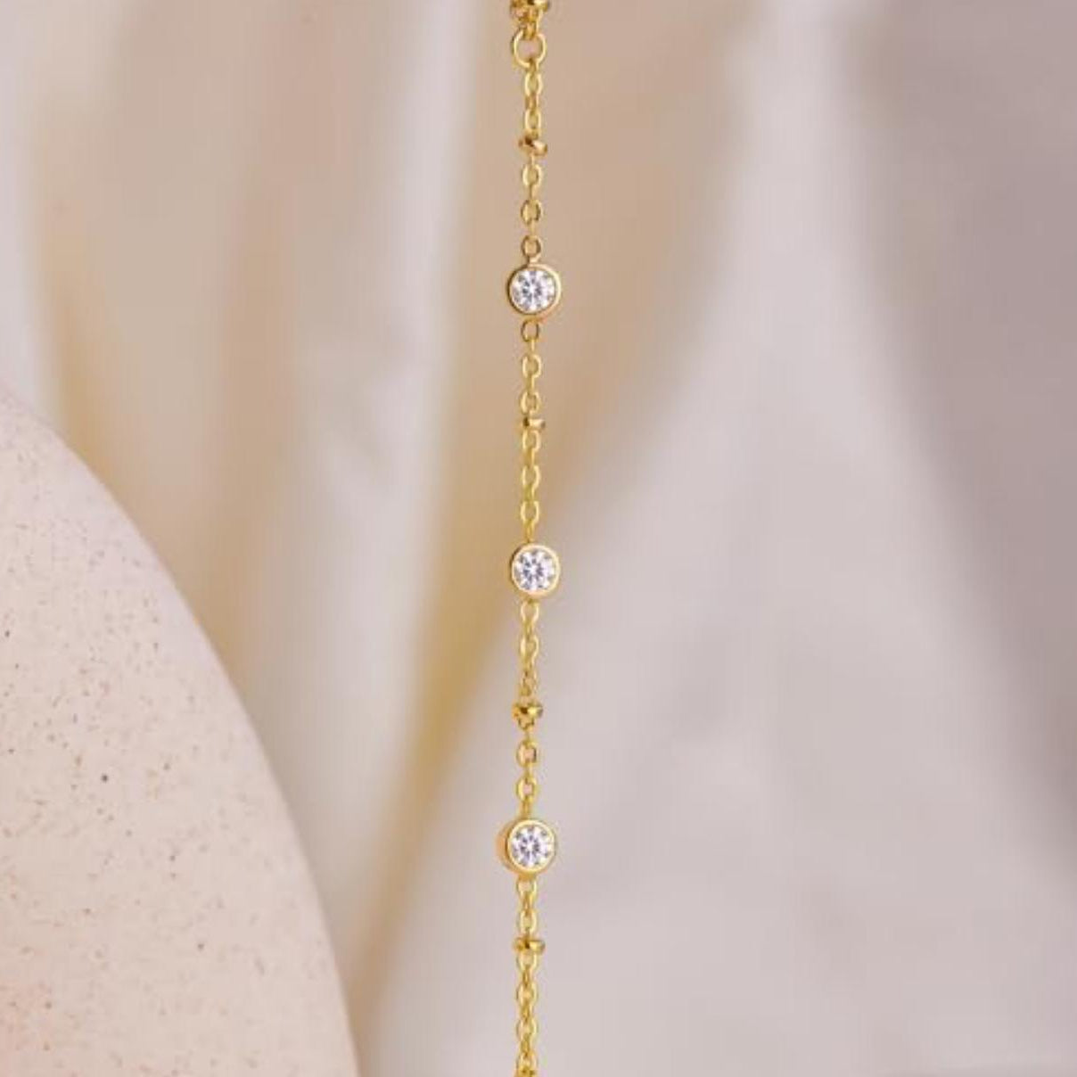 Gold hand chain with round moissanite on a beige background