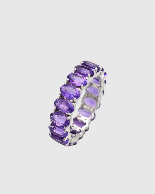 Angled view of the Améthra solid 925 sterling silver eternity band highlighting the 6.7 carats of untreated, oval-cut vibrant purple amethyst stones.