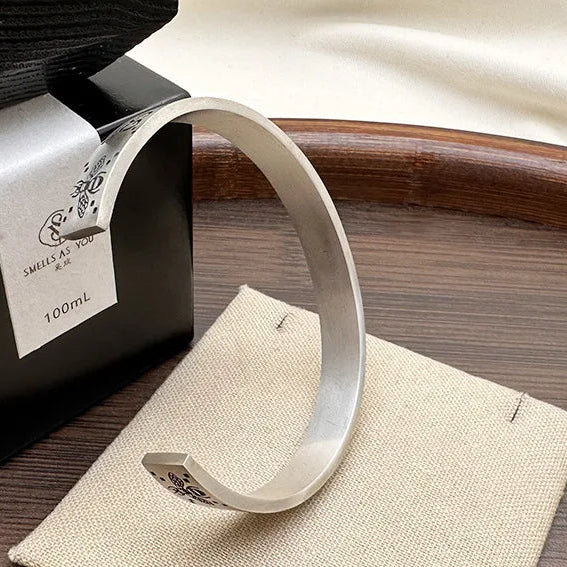 Silver bracelet on a wooden stand with a black container labeled '100mL' in the background.