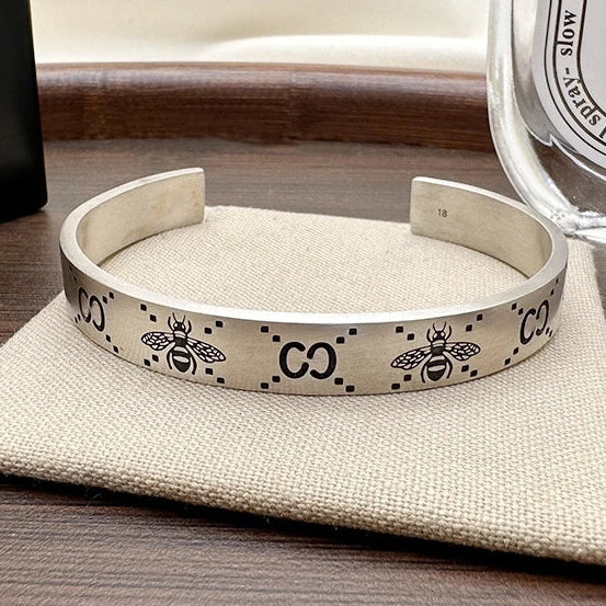 A sterling silver cuff bracelet with a retro bee design, displayed next to its packaging and a perfume bottle.