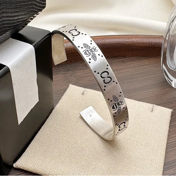 A sterling silver cuff bracelet with a retro bee design, displayed next to its packaging and a perfume bottle.