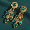 Ornate gold earrings with green gemstones on a green fabric background