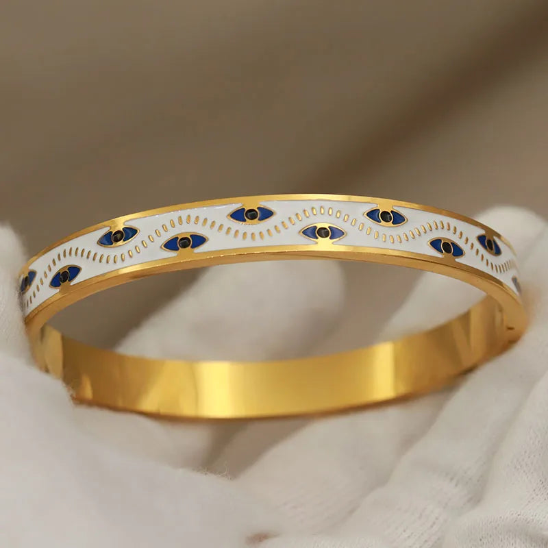 Gold bracelet with blue and black eye designs on a beige background