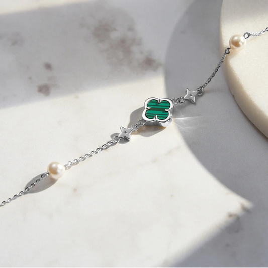 A person's forearm wearing multiple gold-toned bracelets with green malachite and shell pearl accents.