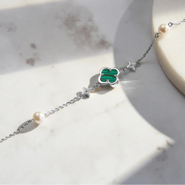 A person's forearm wearing multiple gold-toned bracelets with green malachite and shell pearl accents.