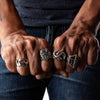Close-up of a person wearing three silver rings on their fingers against a dark background.