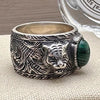 Silver ring with tiger design and green stone on a beige surface
